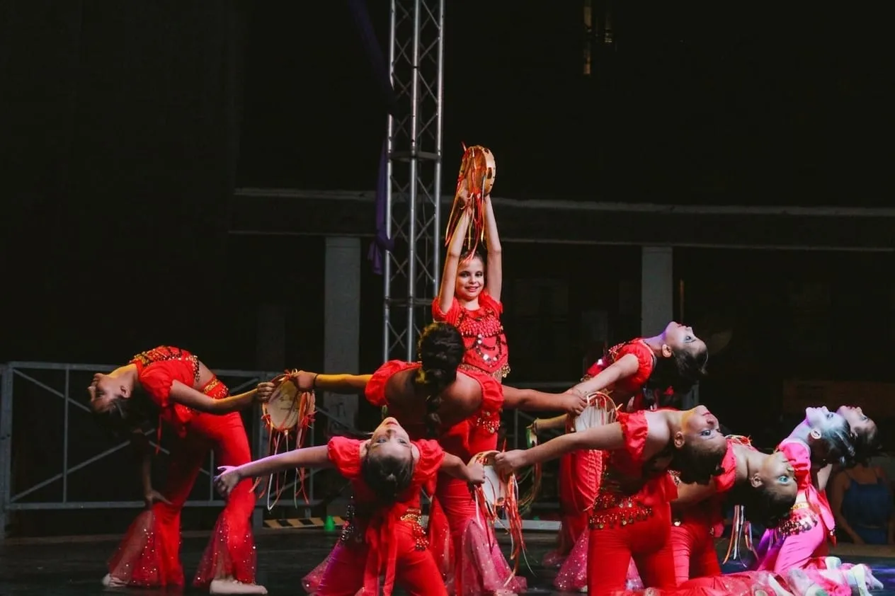 Le allieve di Anima Danzante in costume rosso durante uno spettacolo, con i tamburelli alzati e una ballerina sollevata al centro